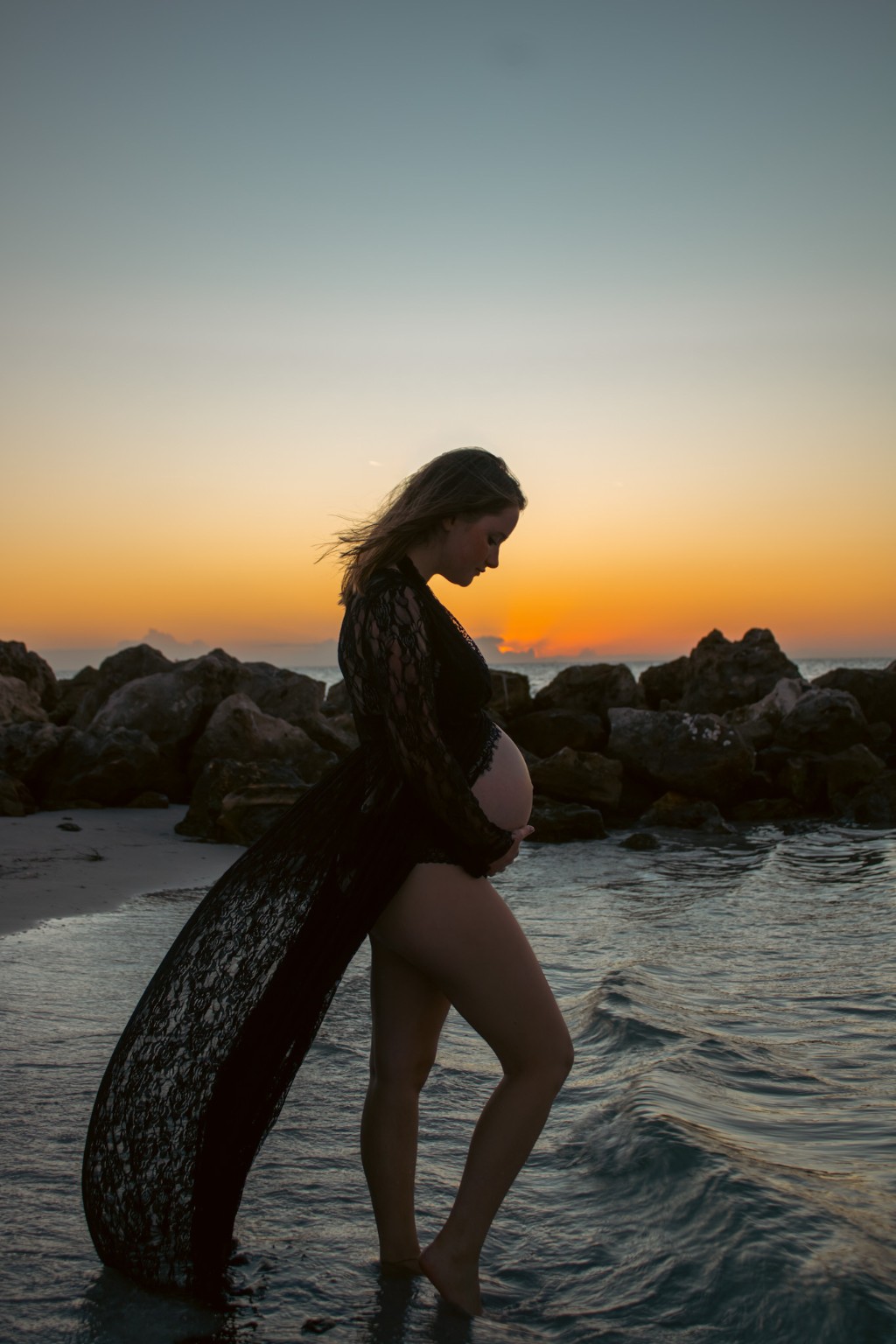 A maternity silhouette beside the ocean at sunset