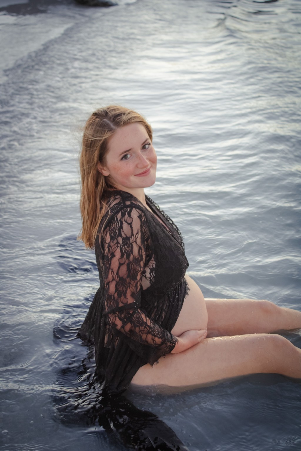 A maternity portrait seated in gentle ocean waves