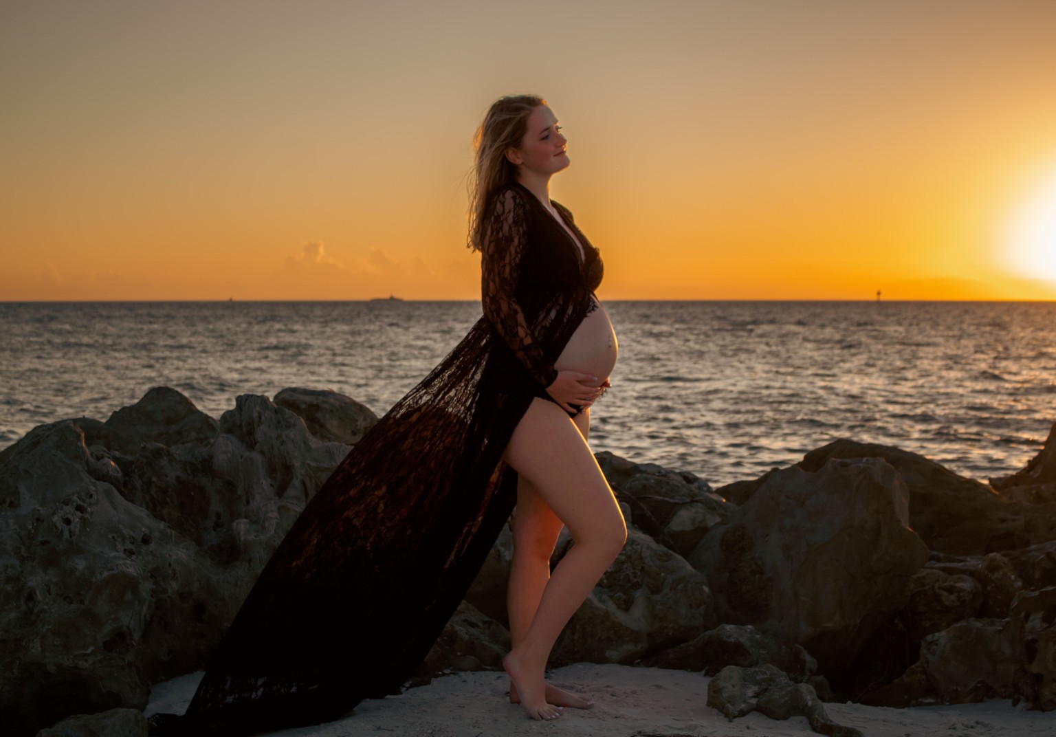 An expectant mother beside the rocks at golden sunset